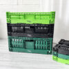 Three green and black plastic crates sitting on a wooden floor.